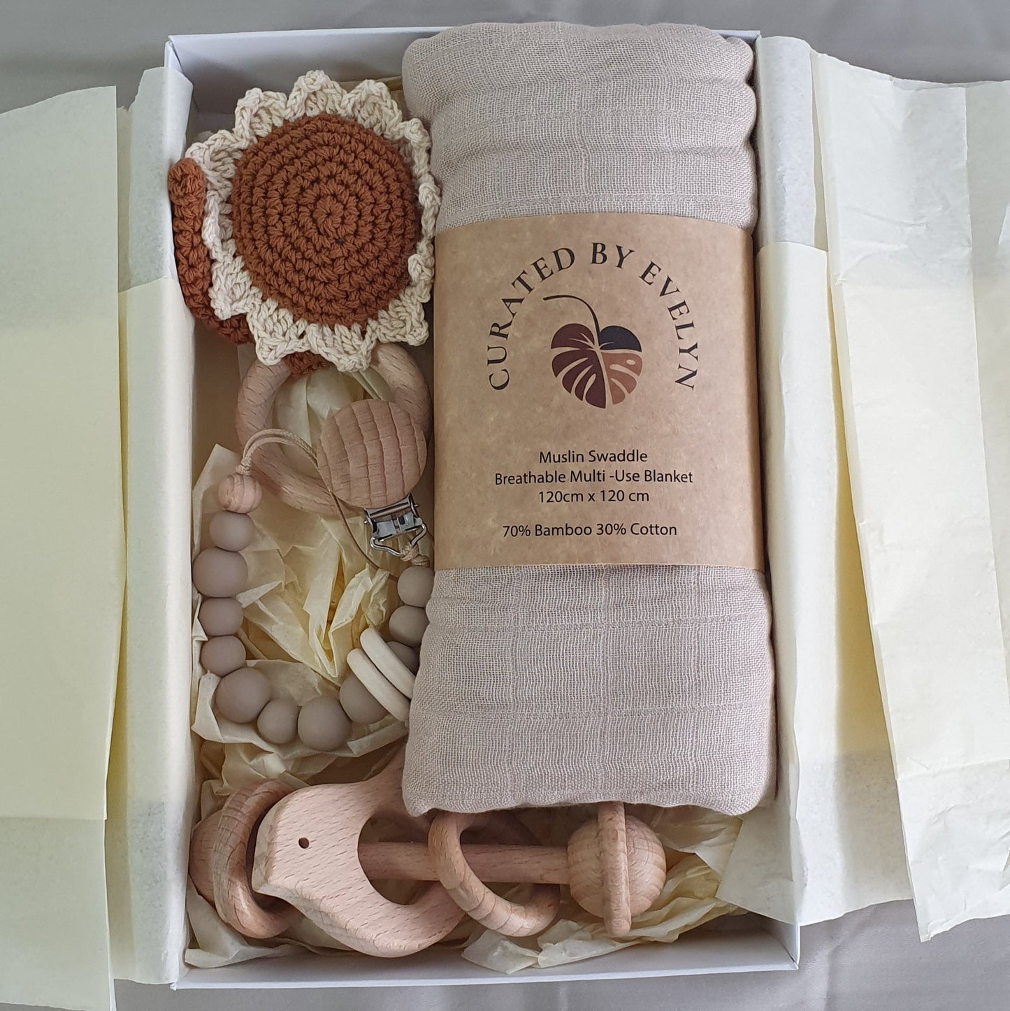 Baby gift set with muslin, two rattles and a comforter clip in a box, including a blanket and toys, on a white background.
